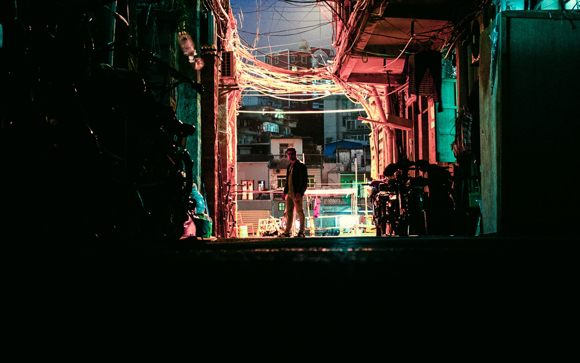 Photo of person standing in an empty street with lots of wires and red lighting